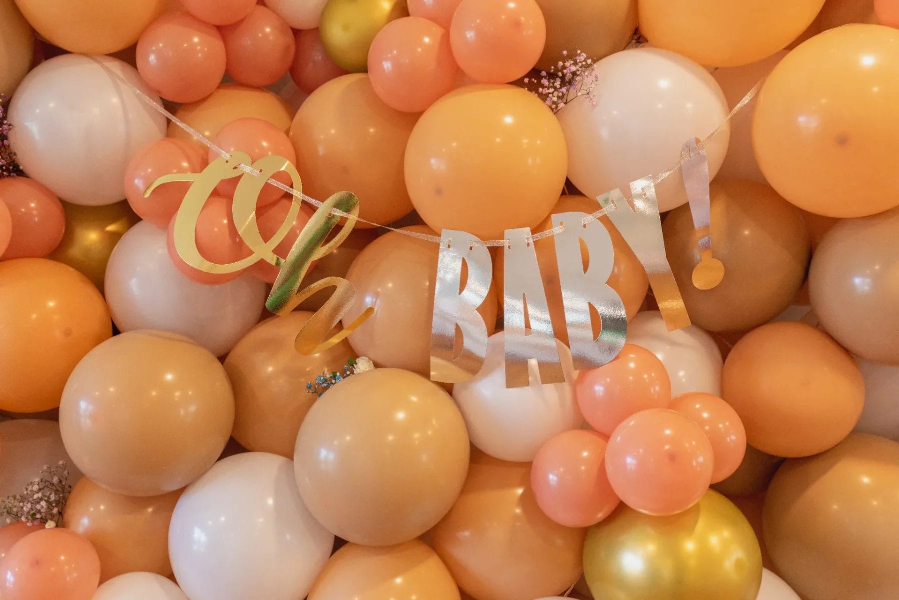 A celebratory arrangement of orange, white, and gold balloons with a shiny banner that reads "Oh BABY!" hanging in the foreground. Huntersville event venue