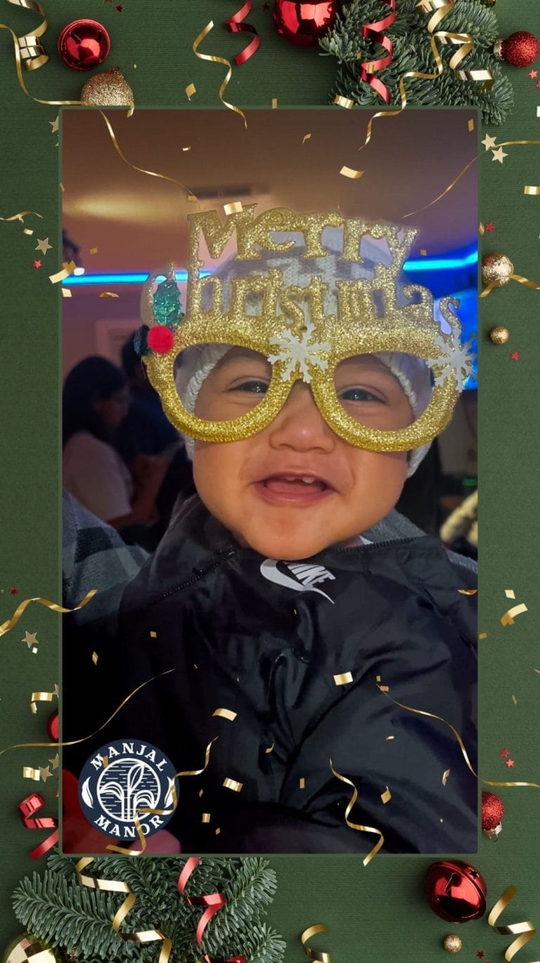A baby wearing oversized "Merry Christmas" glasses smiles joyfully. The background shows a festive atmosphere with people and decorations. Framing the photo are Christmas-themed borders with ornaments and confetti. Huntersville event venue